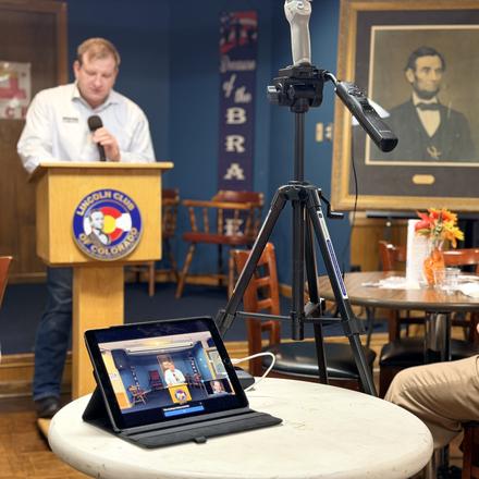 The program at the lectern, streamed on a tablet for members watching remotely