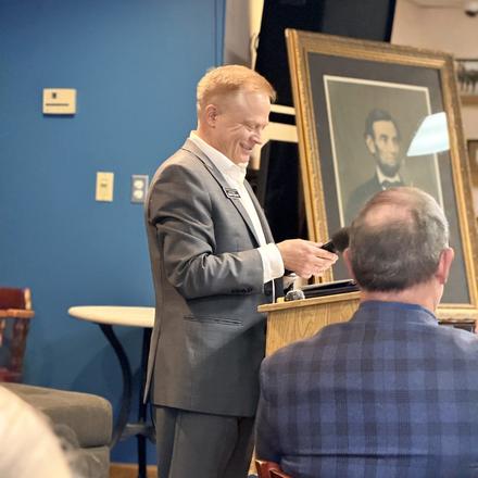 A speaker addressing the room from the lectern beside the Lincoln portrait