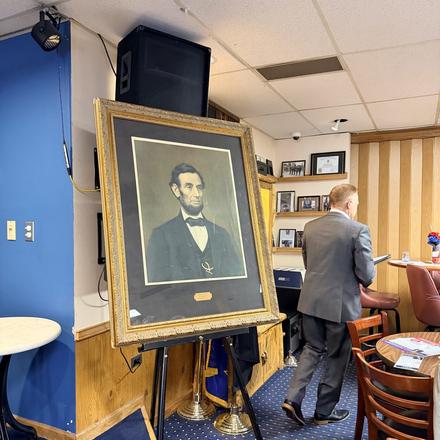The framed portrait of Abraham Lincoln set on an easel at the front of the room
